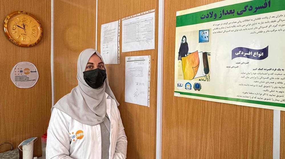 A woman in medical robe standing next a poster on postpartum depression.