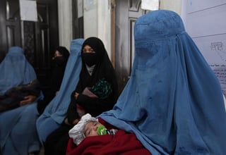 Women wearing burqa carrying their babies sitting outside a clinic.