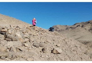 A midwife walking to the top of a rocky hill where a car is parked.