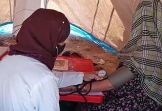 A midwife taking the blood pressure of a mother inside a tent clinic