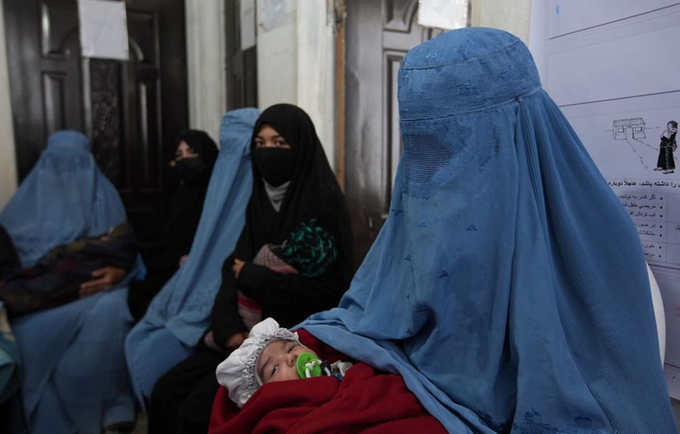Women wearing burqa carrying their babies sitting outside a clinic.