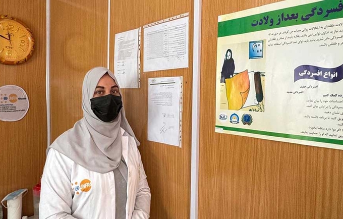 A woman in medical robe standing next a poster on postpartum depression.
