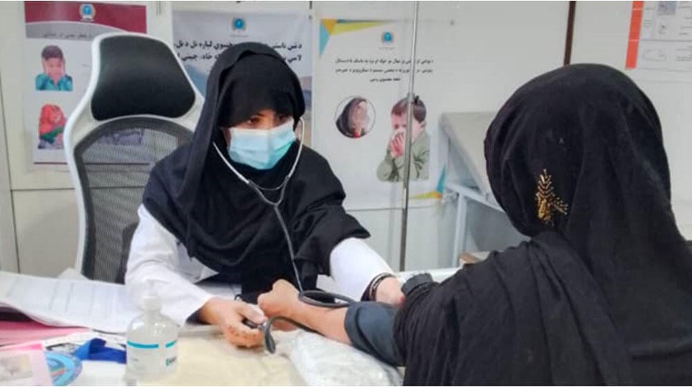 A midwife takes the blood pressure of a female patient inside a clinic