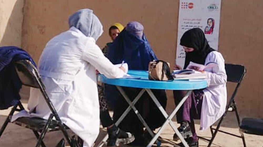 Female health workers with head covering working around a table in an outdoor setting.