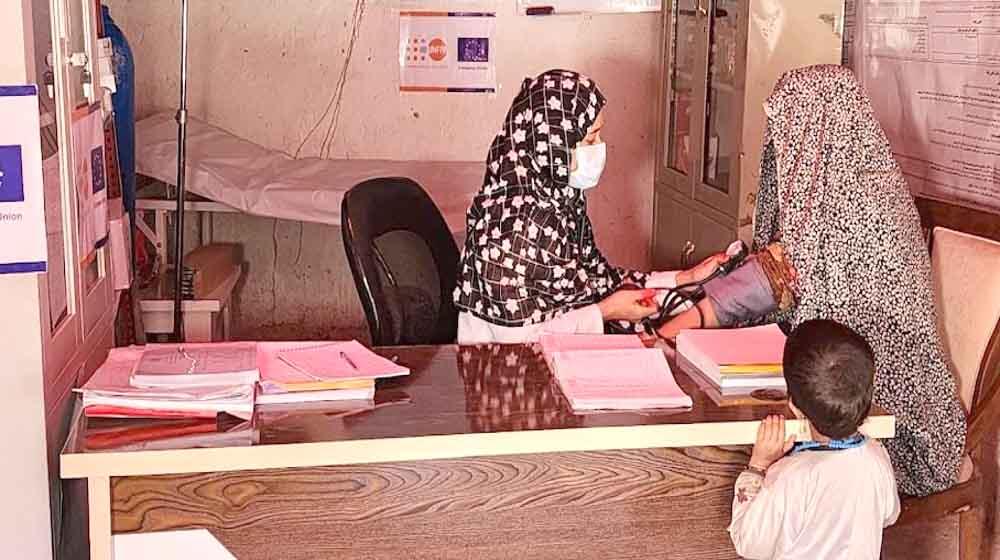 A midwife takes the blood pressure of a woman with burqa while a child watches