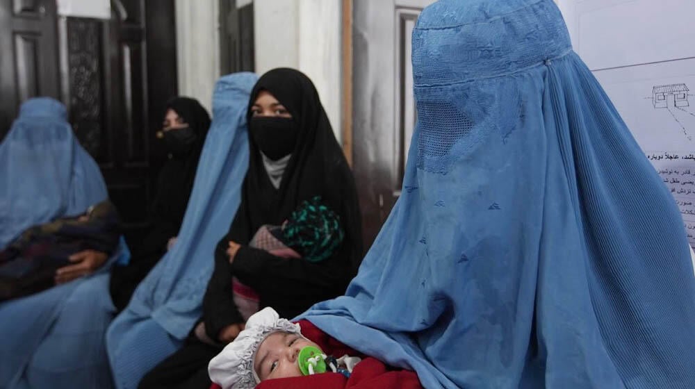 Women wearing burqa wait outside a clinic with their babies.