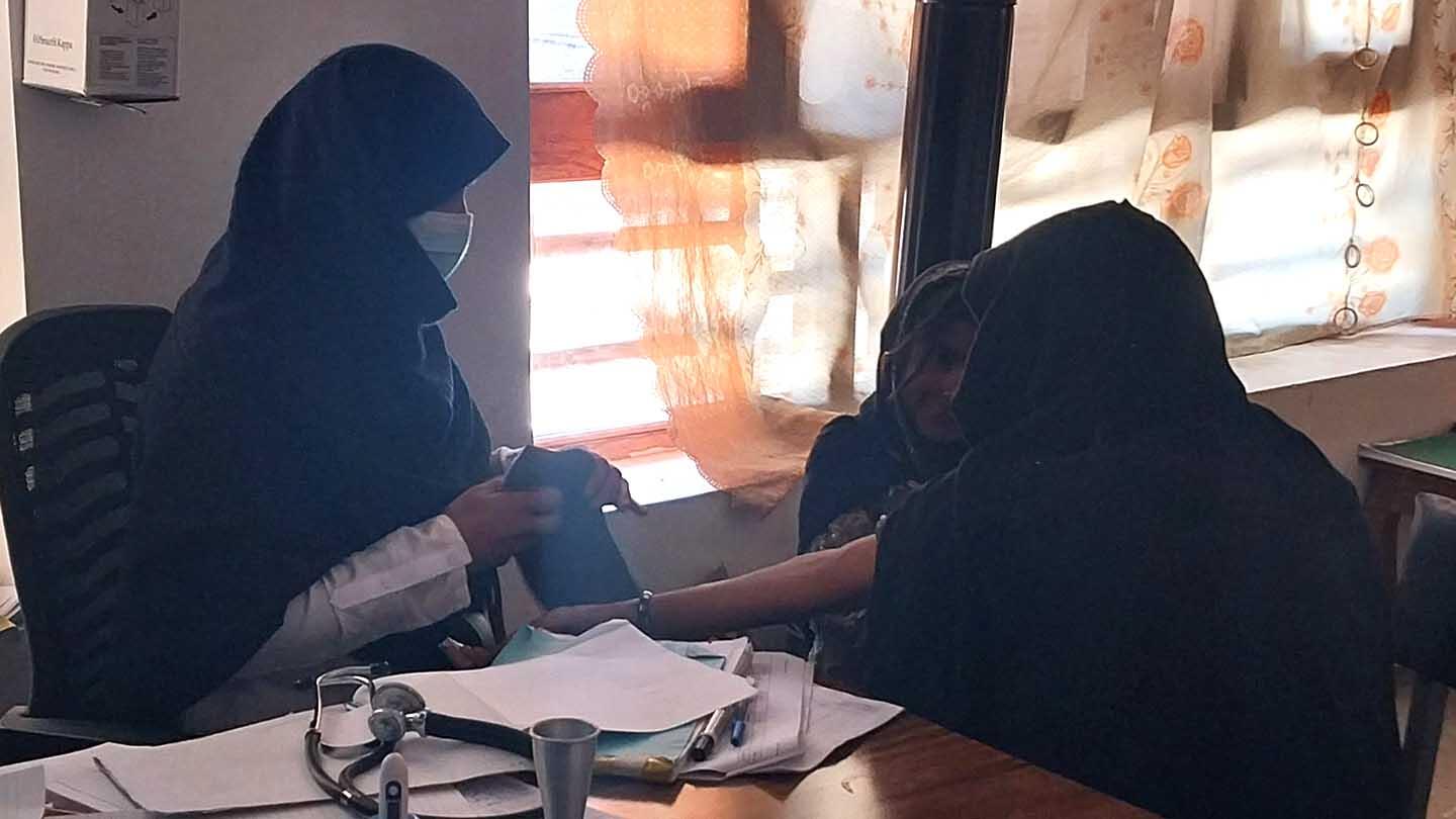 A midwife and a female patient, both wearing black hijabs, inside a clinic.