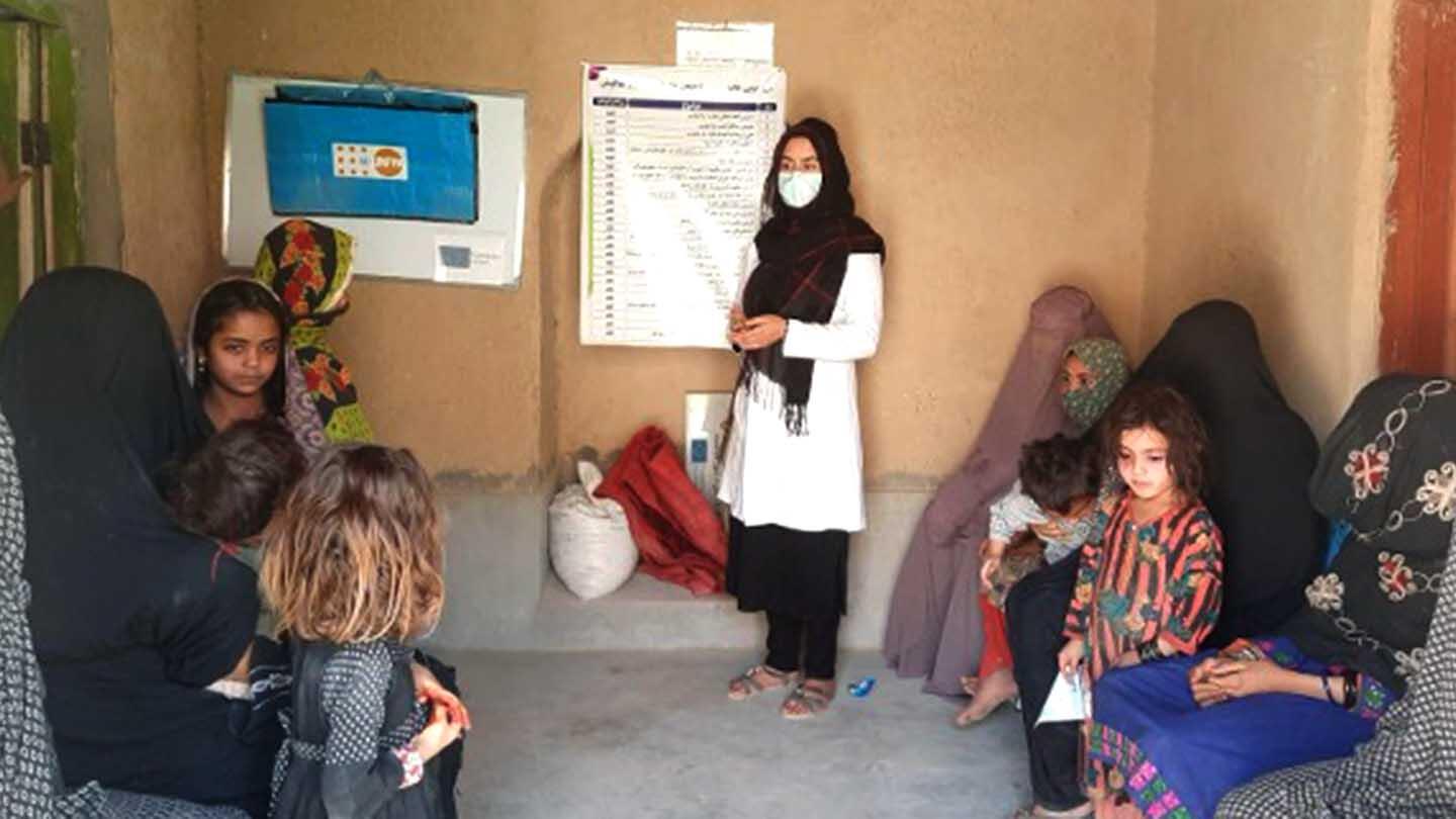 A midwife talking to women and children inside a clinic.