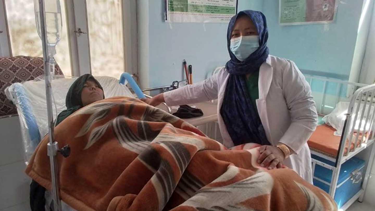 A midwife attending to a woman who is lying in bed inside a clinic.