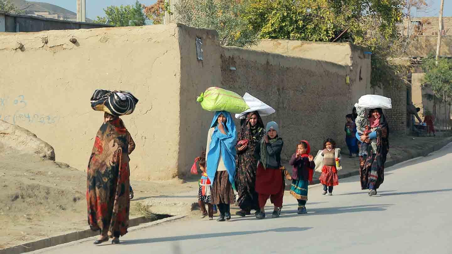 Afghan women and children walking on a street carrying personal belongings on their heads.