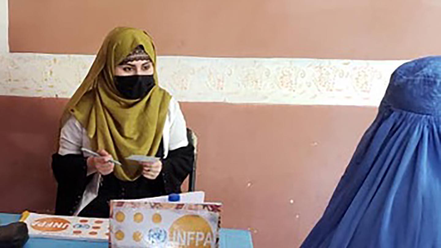 A midwife talks to a woman covered in blue burqa.