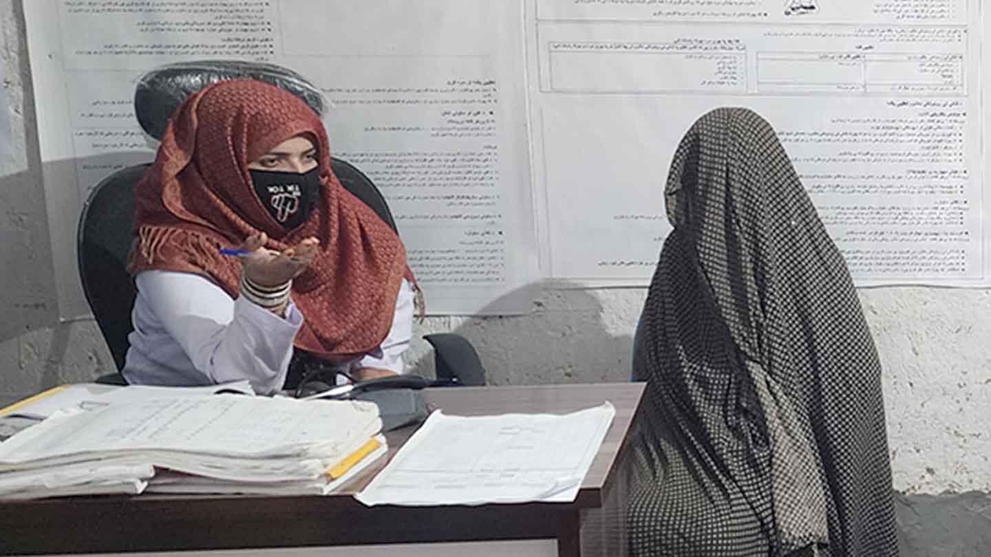 A health worker in red hijab speaks to a woman who is covered from head to toe
