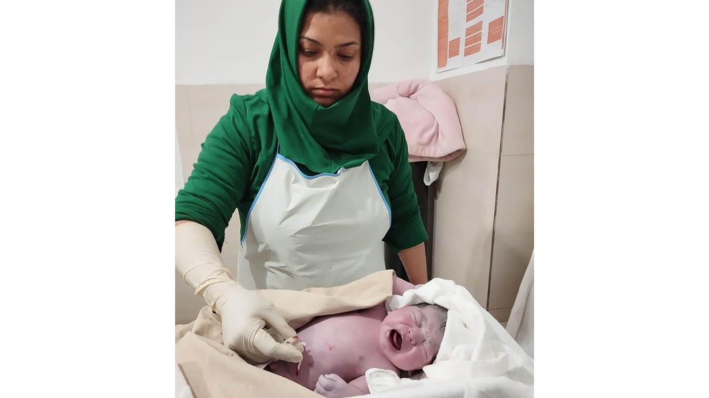 A midwife in green and white uniform cleaning up a newborn baby