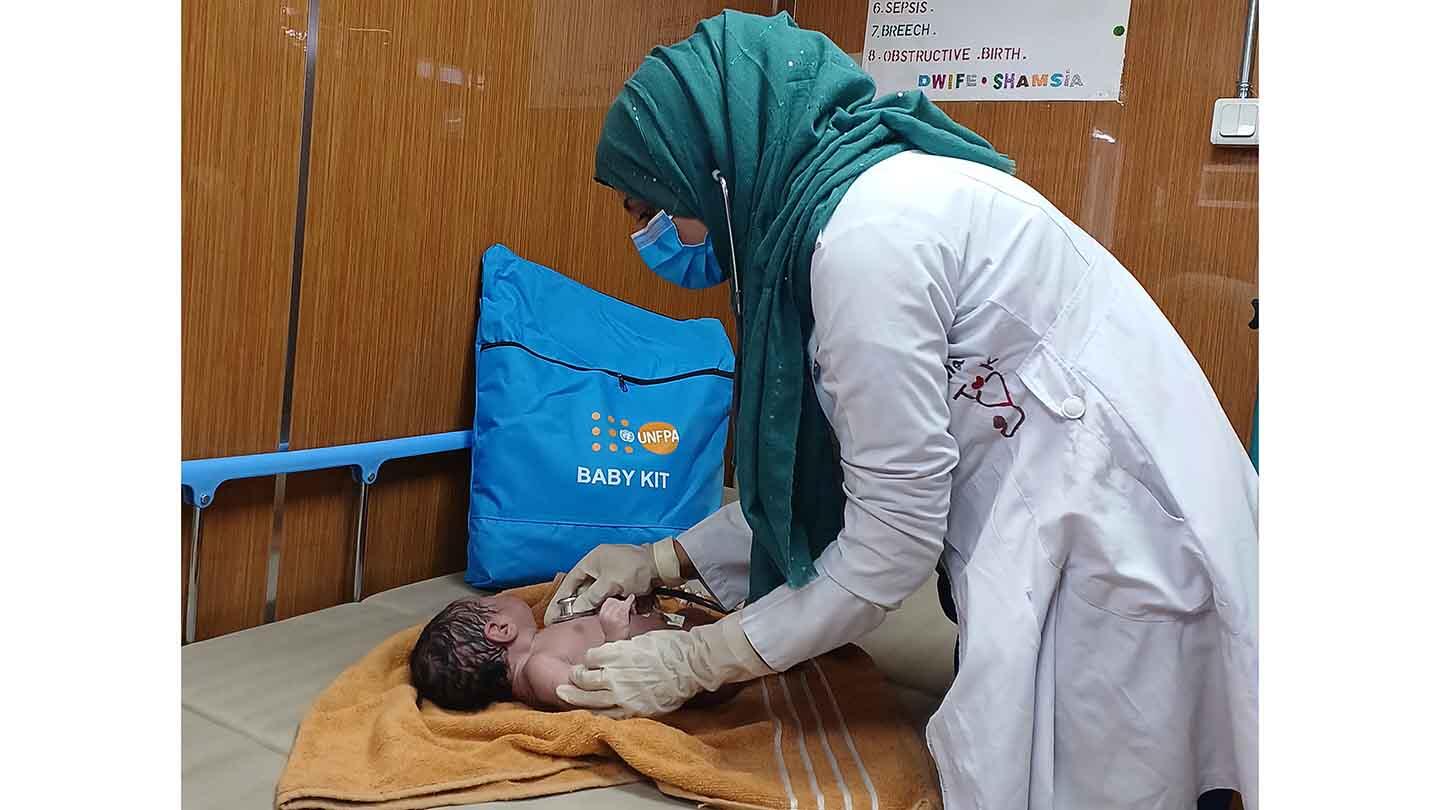 A midwife in white uniform cleans up a newborn baby.