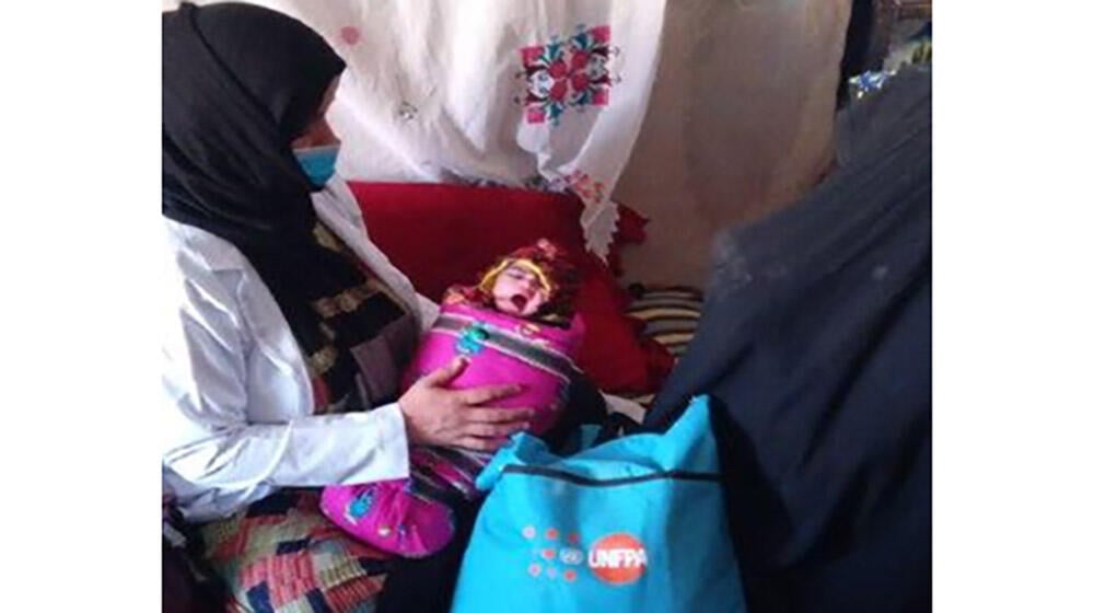 A midwife holding a baby with the mother in front of them.