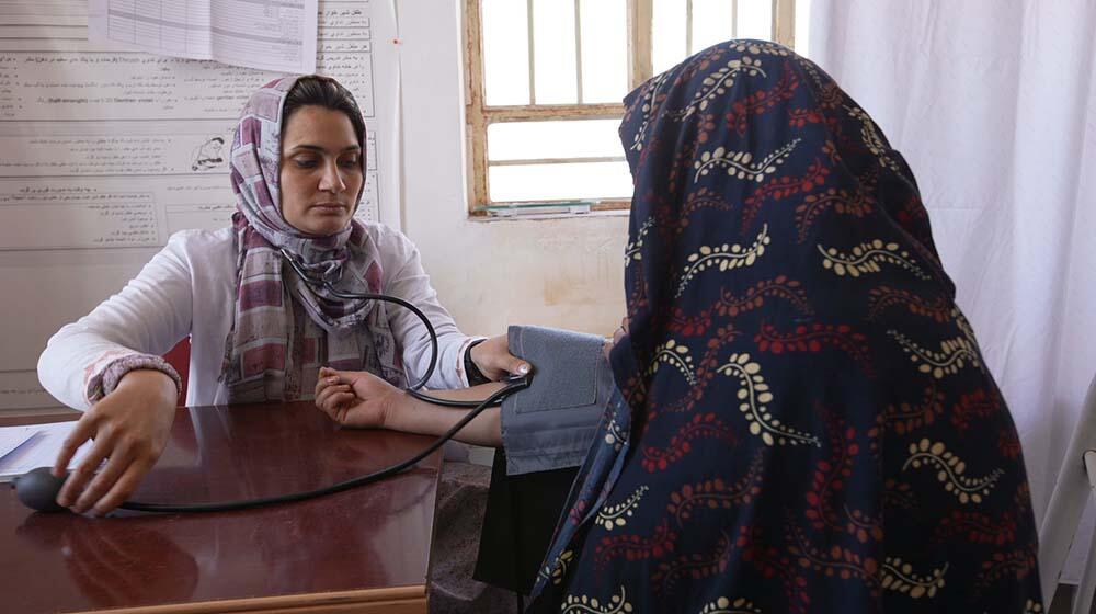 A midwife takes the blood pressure of a woman in hijab.