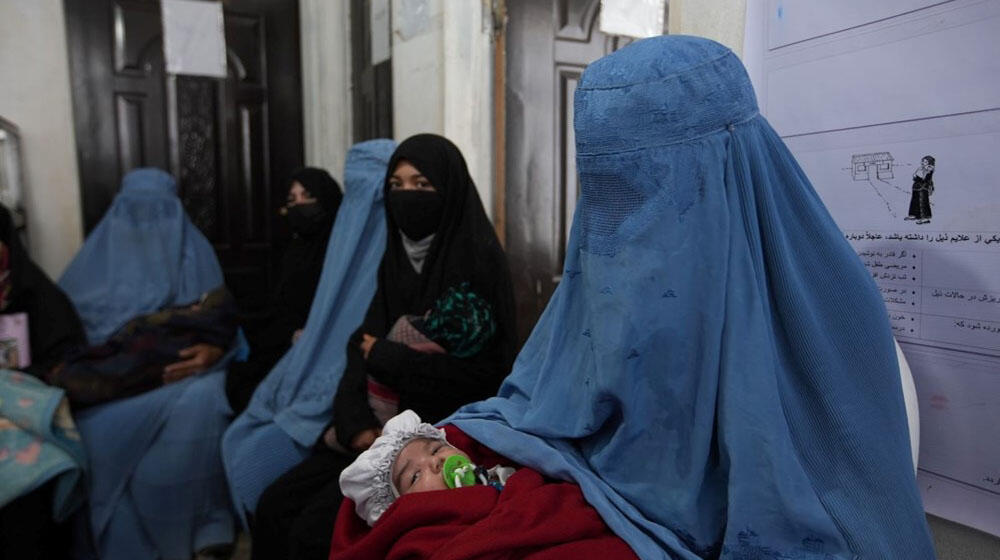 Women wearing burqa carrying their babies sitting outside a clinic.