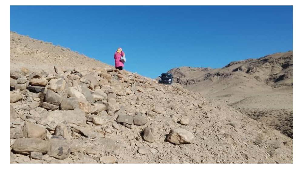 A midwife walking to the top of a rocky hill where a car is parked.