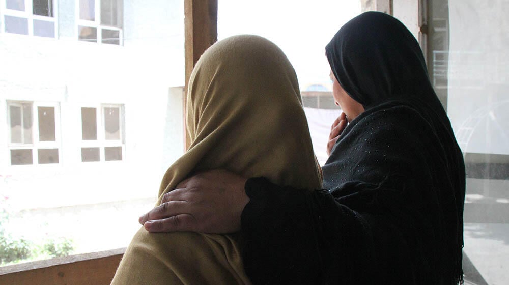 Silhouette of two women staring out a window.